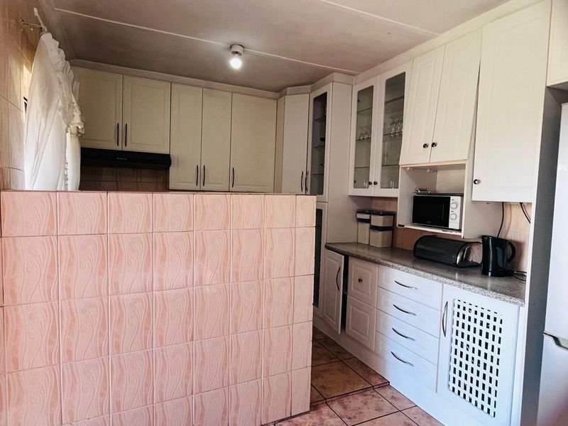 A functional kitchen featuring white built-in cabinetry, laminate countertops, and a tiled partition wall, offering ample storage and preparation space.