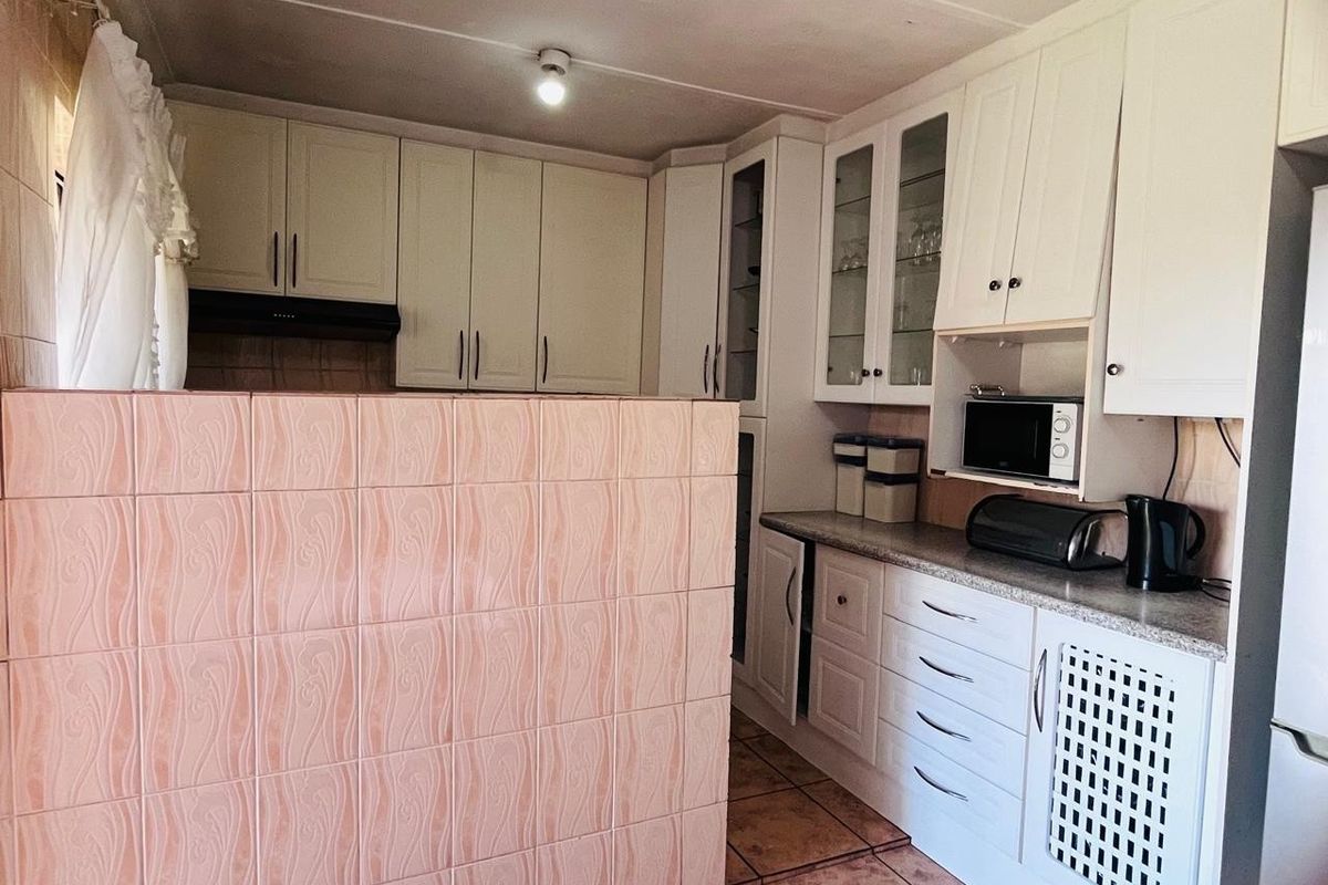 A functional kitchen featuring white built-in cabinetry, laminate countertops, and a tiled partition wall, offering ample storage and preparation space.