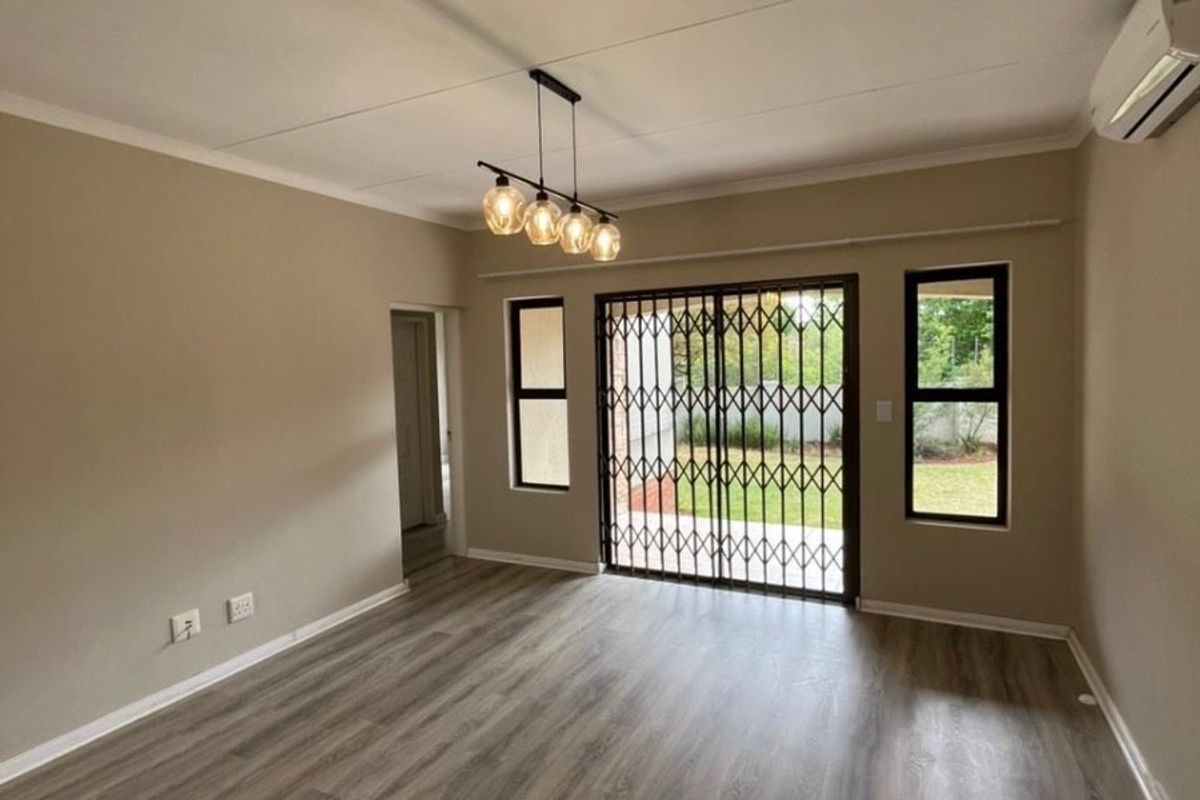 A bright and spacious living area featuring modern laminate flooring, an air conditioning unit, and sliding doors leading to the garden.