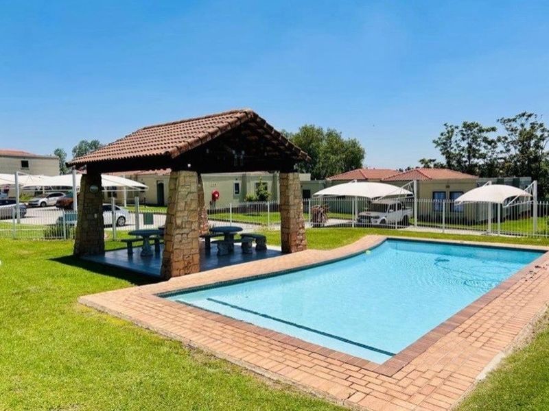 Outdoor pool area featuring a swimming pool with brick coping and a covered thatched gazebo with stone pillars set in a landscaped garden.