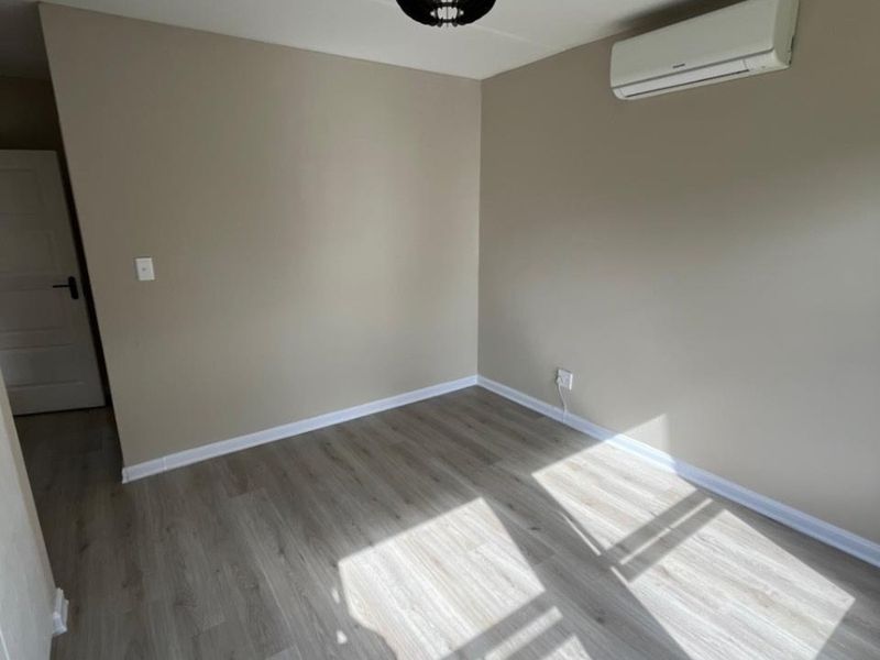 A bright, empty bedroom featuring modern laminate flooring, neutral wall tones, and a wall-mounted air conditioning unit.