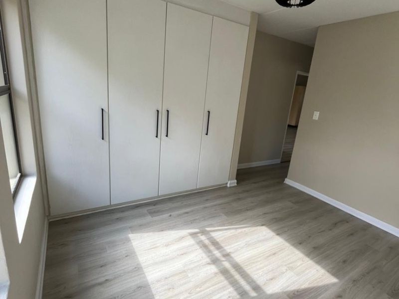 A bright, empty bedroom featuring modern laminate flooring and ample built-in cupboard storage space.