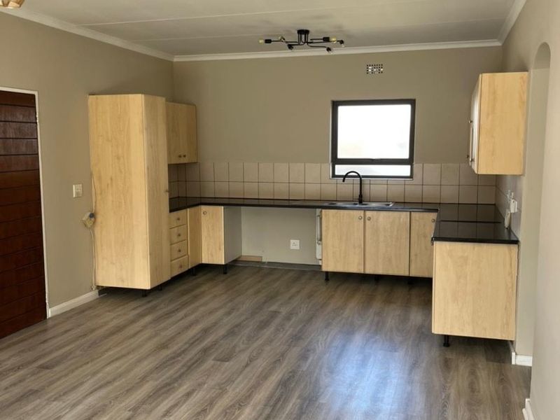 A clean, empty kitchen featuring light wood-look cabinetry, black granite countertops, a tiled backsplash, and modern laminate flooring.