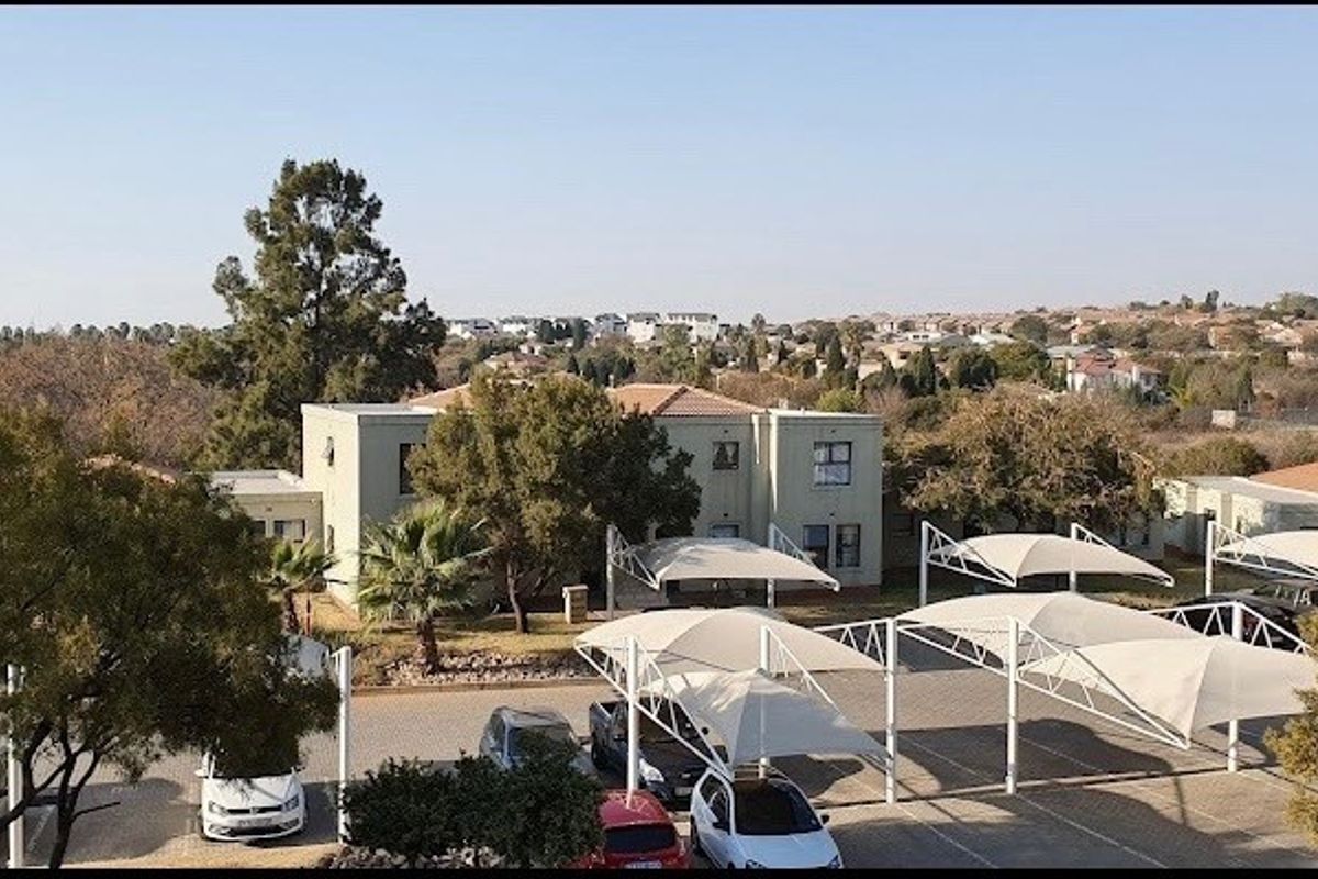 An elevated view of the property grounds featuring a paved parking area with multiple shade cloth carports and surrounding landscaped garden space.