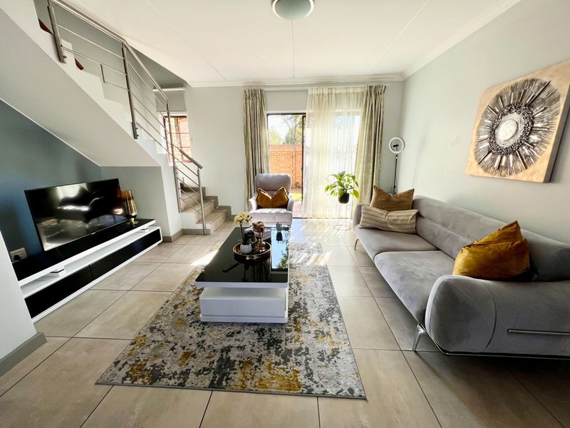 A bright and modern living room featuring tiled flooring, a staircase with a stainless steel balustrade, and sliding glass doors leading to the exterior.
