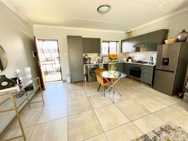 Open-plan kitchen featuring modern grey cabinetry, tiled flooring, and integrated appliances, with direct access to an exterior security gate.