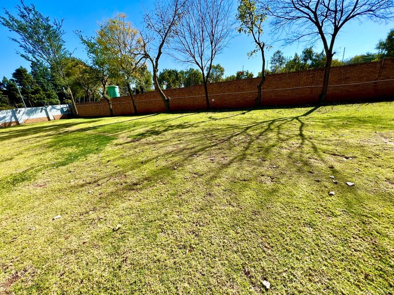 A spacious backyard featuring a large lawn area enclosed by a brick boundary wall with integrated electric fencing and a water tank.
