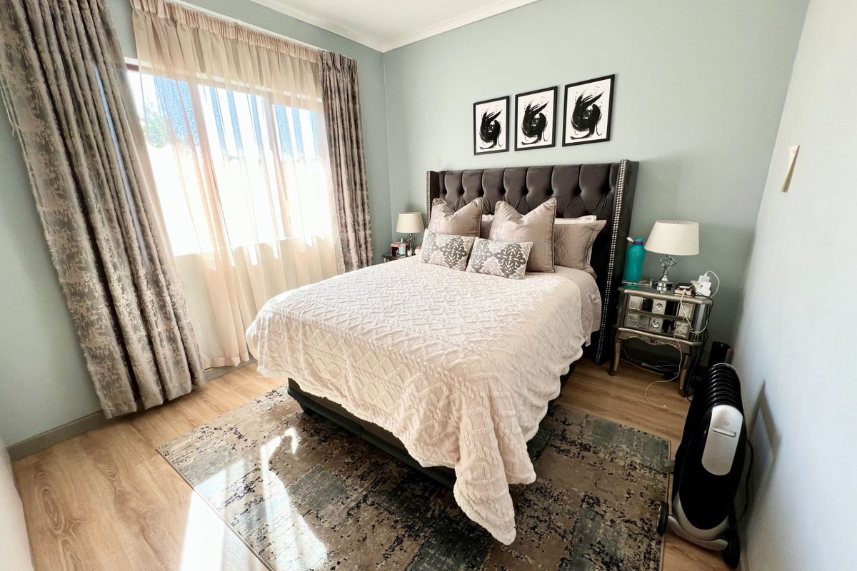 A well-maintained bedroom featuring light-toned laminate flooring, coved ceilings, and a large window with natural light.