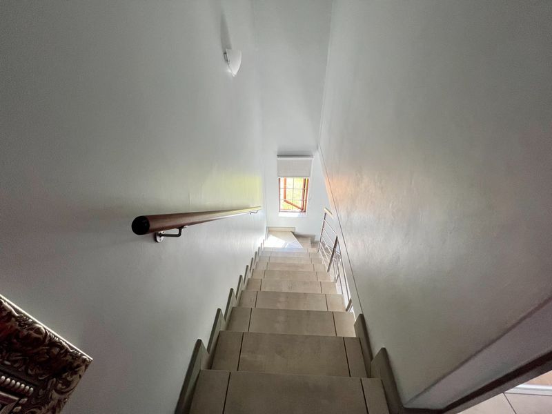A clean, well-lit staircase featuring tiled steps, a wooden handrail, and a window at the landing.