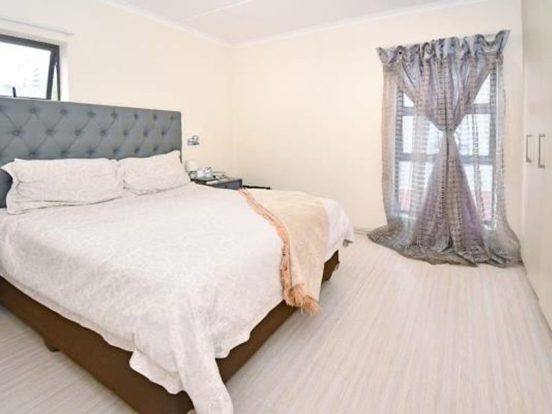 A well-maintained bedroom featuring light-toned flooring, built-in cupboards, and natural light from dual windows.