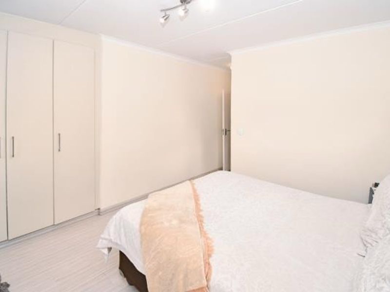 A well-maintained bedroom featuring neutral walls, light-toned flooring, and ample built-in cupboard storage with modern track lighting.