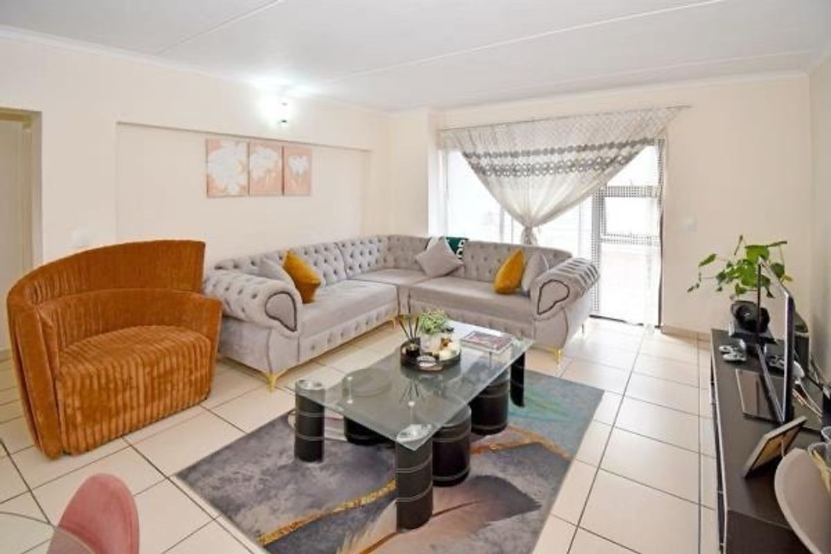 A well-maintained living room featuring neutral tiled flooring and a sliding glass door providing natural light.