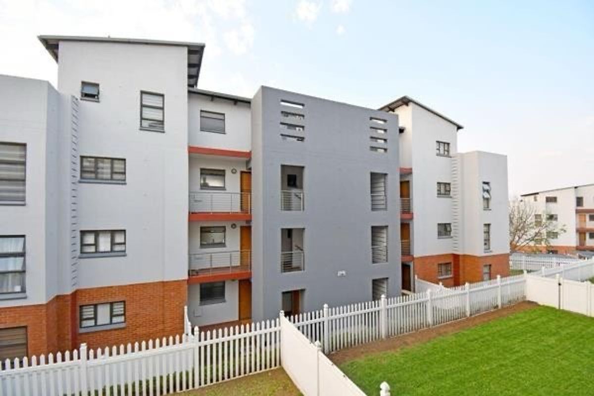A view of the rear elevation of a modern apartment complex featuring multi-level balconies, brick and plaster finishes, and a well-maintained lawn with fencing.