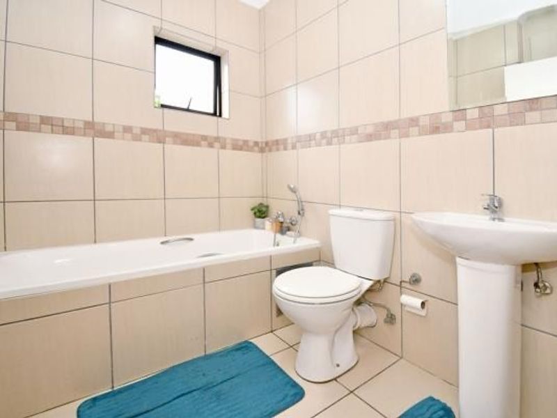 A functional bathroom featuring a bathtub, pedestal basin, and toilet with neutral wall and floor tiling.