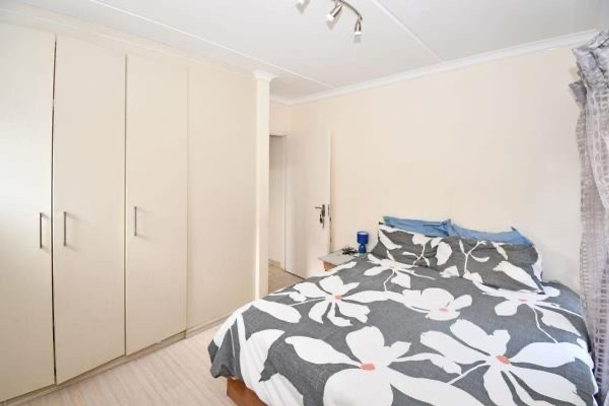 A bedroom featuring built-in cupboards, cove cornicing, and track lighting, providing a functional and neutral space.