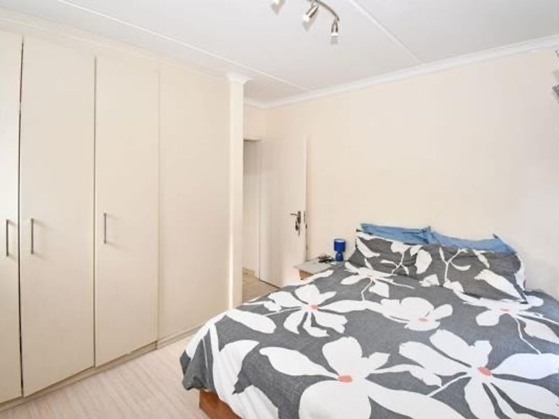 A bedroom featuring built-in cupboards, cove cornicing, and track lighting, providing a functional and neutral space.