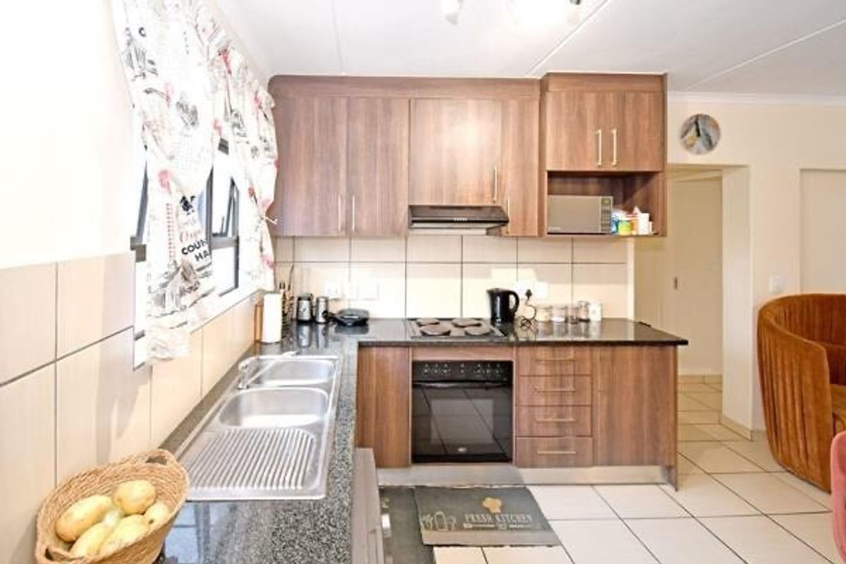 A functional kitchen featuring wood-finish cabinetry, granite countertops, a double basin sink, and integrated appliances including an oven and hob.