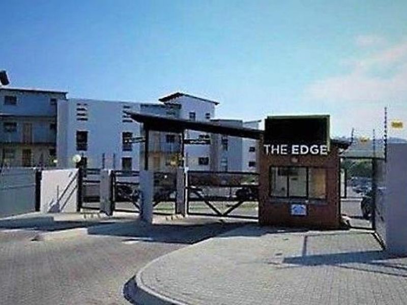 The secure entrance and guard house of The Edge apartment complex, featuring paved access and perimeter electric fencing.