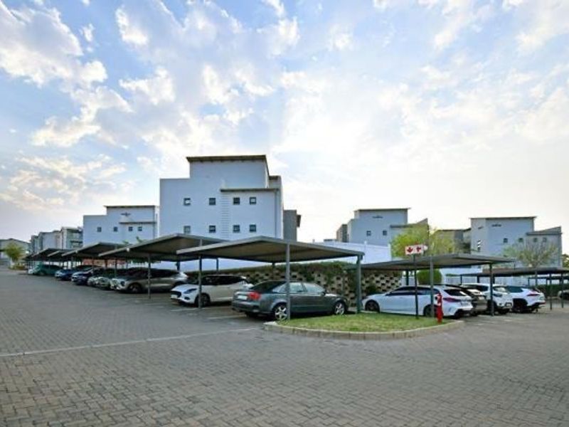Exterior view of the apartment complex featuring paved driveway and multiple covered parking bays for residents.