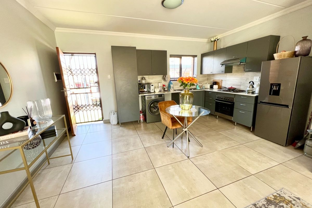 Modern open-plan kitchen featuring sleek grey cabinetry, tiled flooring, and integrated appliances, with direct access to an exterior security gate.