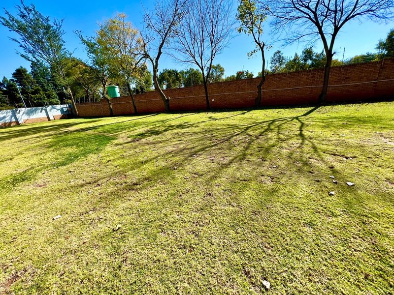 A spacious, level garden area featuring a brick boundary wall with integrated electric fencing and a water tank.