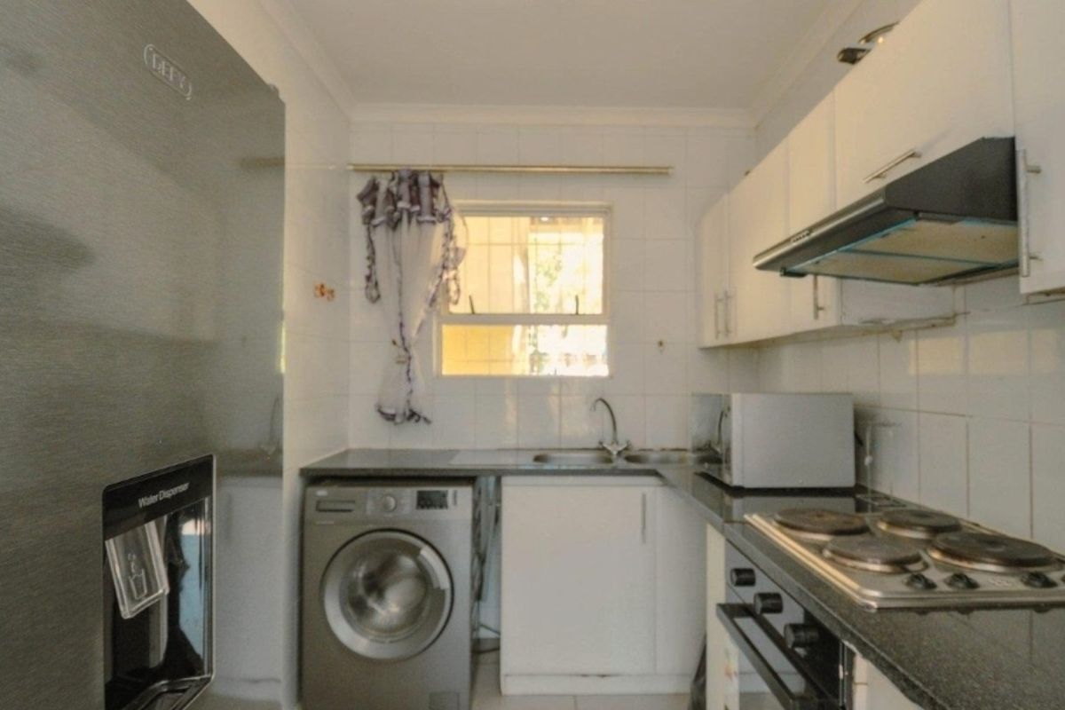 Compact kitchen featuring white cabinetry, granite countertops, built-in oven, electric hob, extractor fan, and integrated laundry plumbing.