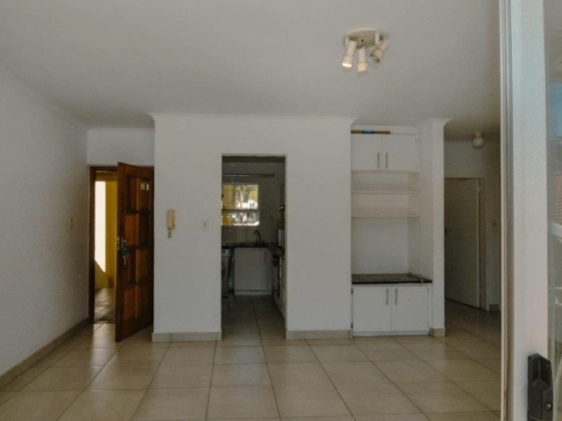 An open-plan living area featuring neutral tiled flooring, built-in storage cabinetry, and direct access to the kitchen and entrance hallway.