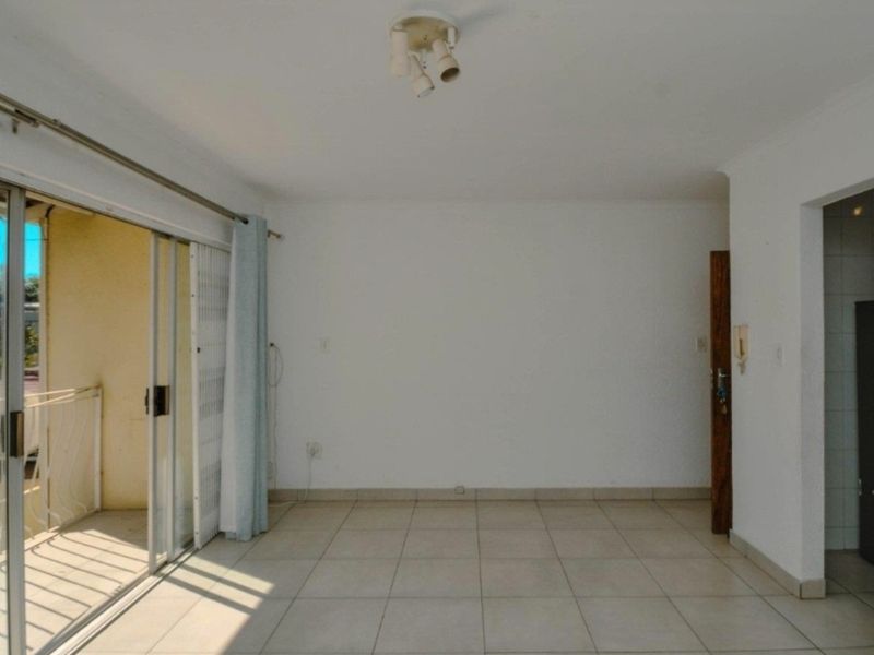 An empty, tiled living room featuring a sliding glass door that opens onto a balcony, providing natural light and access to outdoor space.