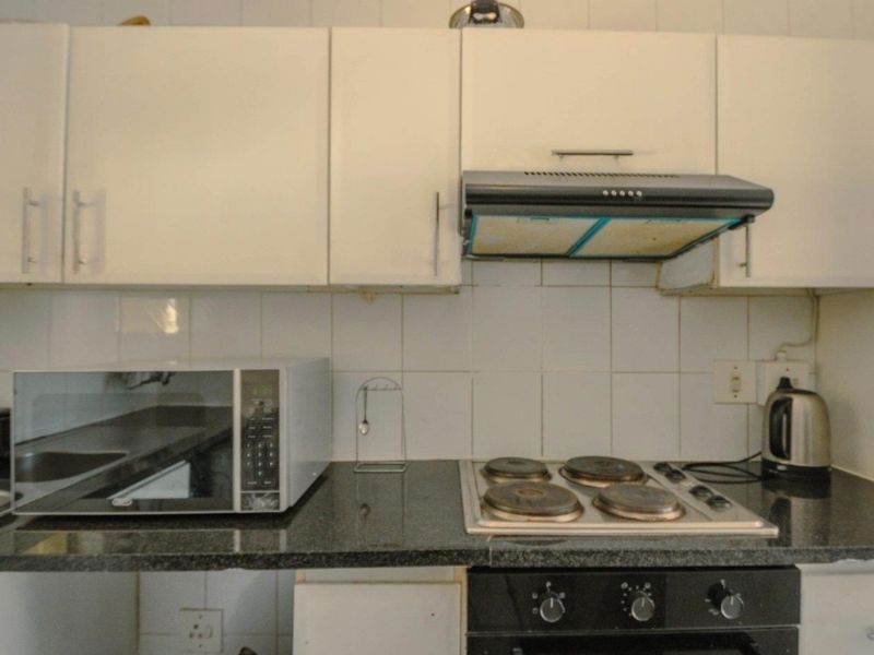 A compact kitchen featuring white cabinetry, granite countertops, a tiled backsplash, and integrated cooking appliances including an electric hob and oven.