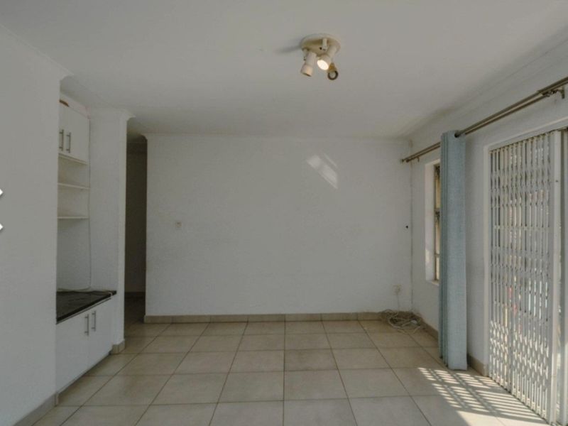 An empty living room featuring tiled flooring, built-in cabinetry, and a sliding glass door with a security gate leading to an outdoor area.