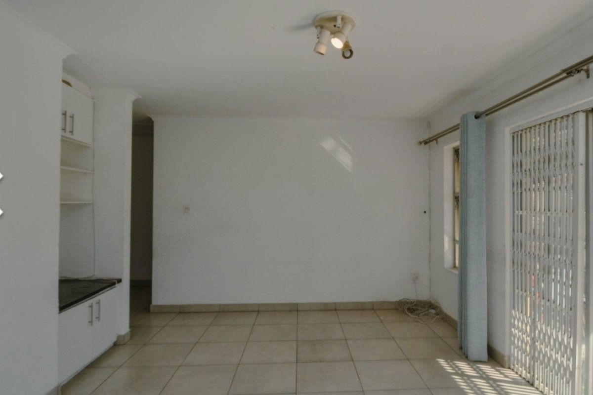 An empty living room featuring tiled flooring, built-in cabinetry, and a sliding glass door with a security gate leading to an outdoor area.
