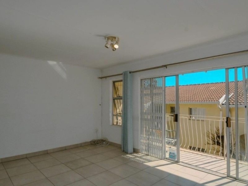 An empty living room featuring tiled flooring and a sliding glass door that opens onto a balcony, providing natural light.