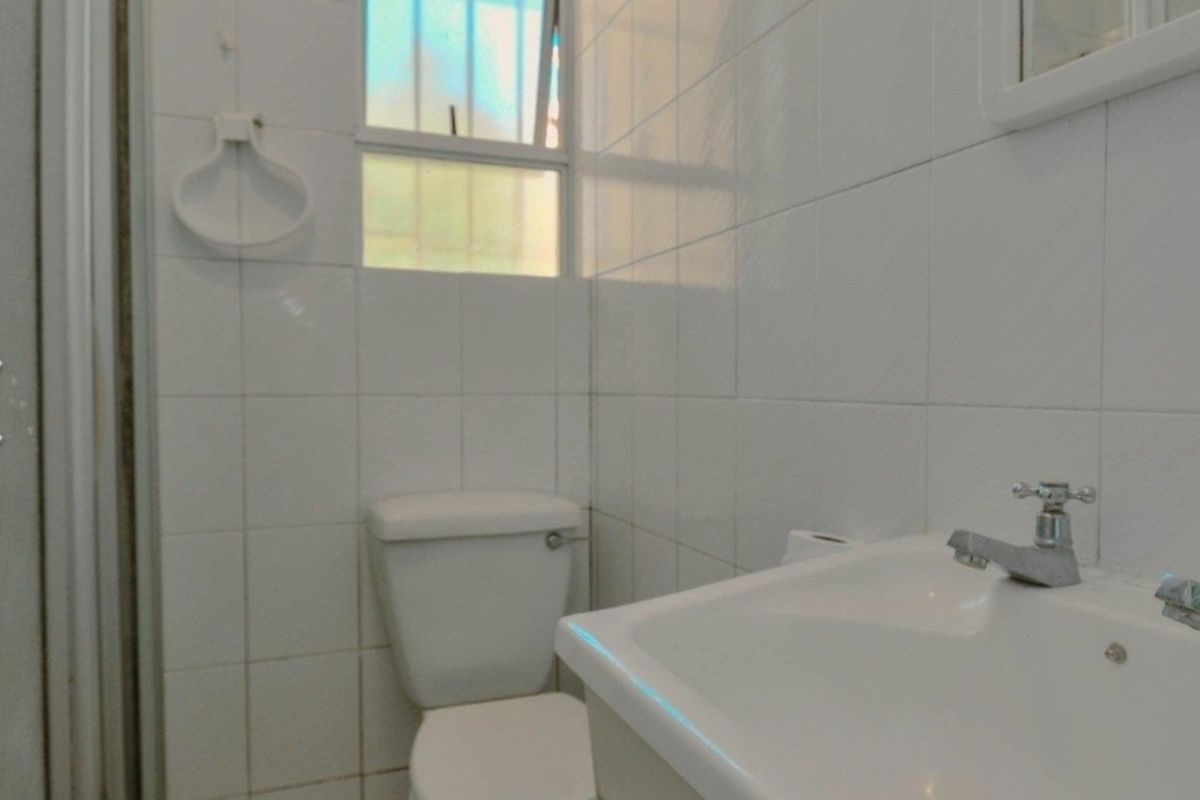 A functional bathroom featuring white wall tiles, a standard toilet, a vanity washbasin, and a shower enclosure.