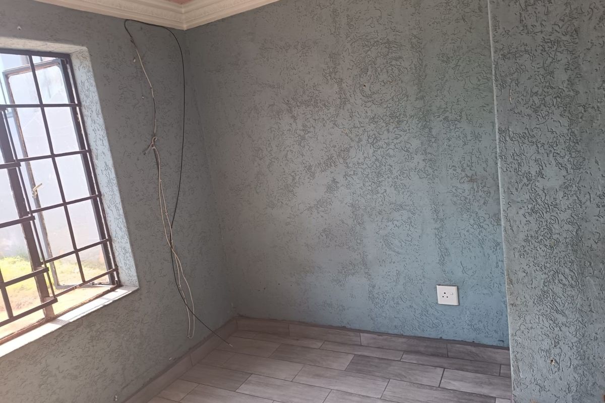 An empty bedroom featuring textured blue walls, tiled flooring, and decorative coving, with visible exposed wiring requiring attention.