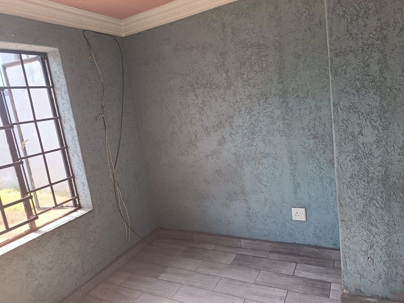 An empty bedroom featuring textured blue walls, tiled flooring, and decorative coving, with visible exposed wiring requiring attention.