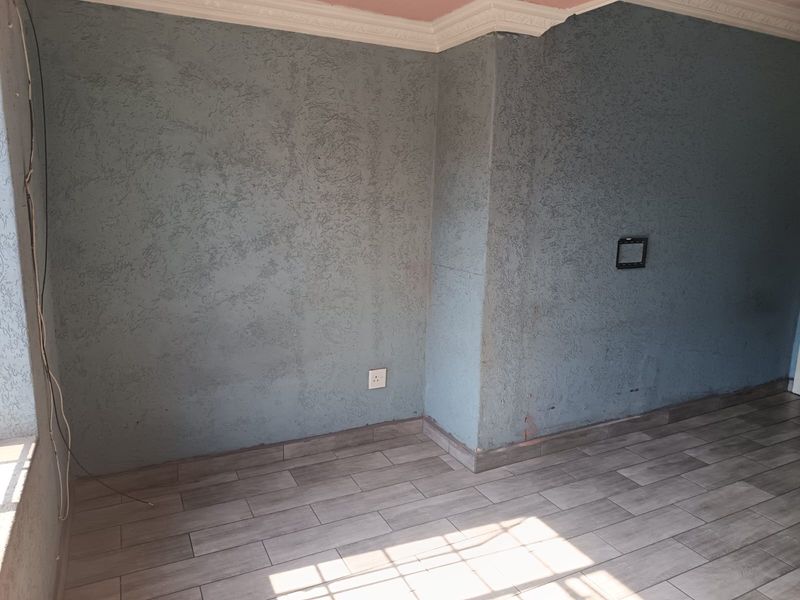 An empty living area featuring textured blue walls, crown molding, and modern wood-look floor tiles, providing a blank canvas for interior design.
