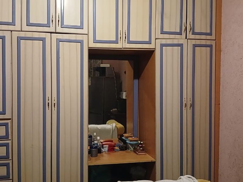 A bedroom featuring a large, multi-section built-in wardrobe with an integrated vanity mirror and an arched doorway leading to the adjacent space.