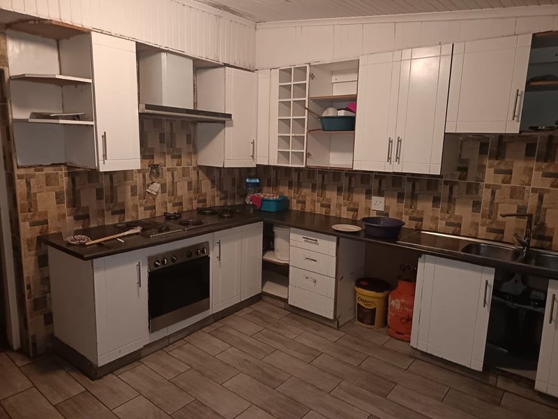 A functional kitchen featuring white cabinetry, built-in oven, gas hob, and tiled backsplash, currently requiring some maintenance and cosmetic updates.