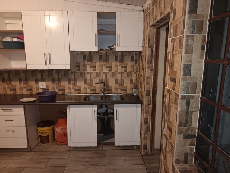 Kitchen area featuring white cabinetry, tiled backsplash, and double bowl sink, currently requiring completion of cabinet installation and plumbing finishing.