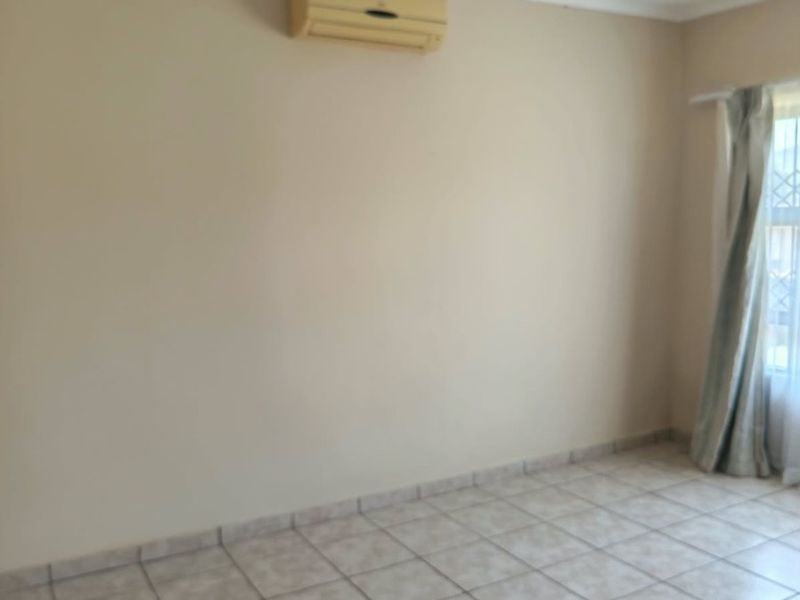 An empty bedroom featuring tiled flooring and a wall-mounted air conditioning unit, providing a neutral canvas for personalization.