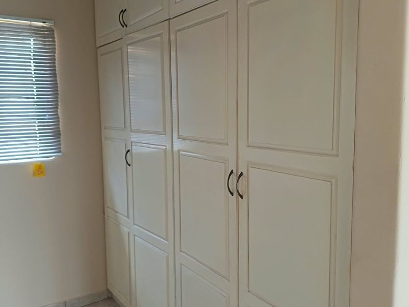 A clean, empty bedroom featuring ample built-in cupboard storage, neutral tiled flooring, and window blinds.