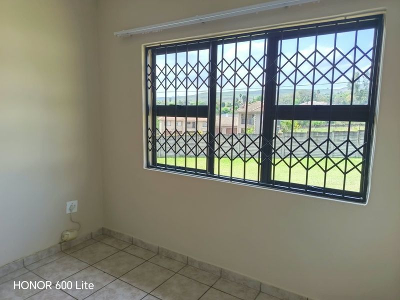 A vacant bedroom featuring tiled flooring and a window fitted with a security gate, offering a view of the surrounding neighborhood.