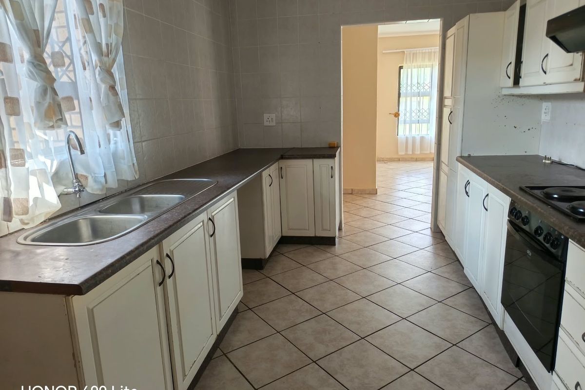A functional kitchen featuring built-in cabinetry, laminate countertops, a double sink, and integrated oven and hob with tiled flooring and splashbacks.