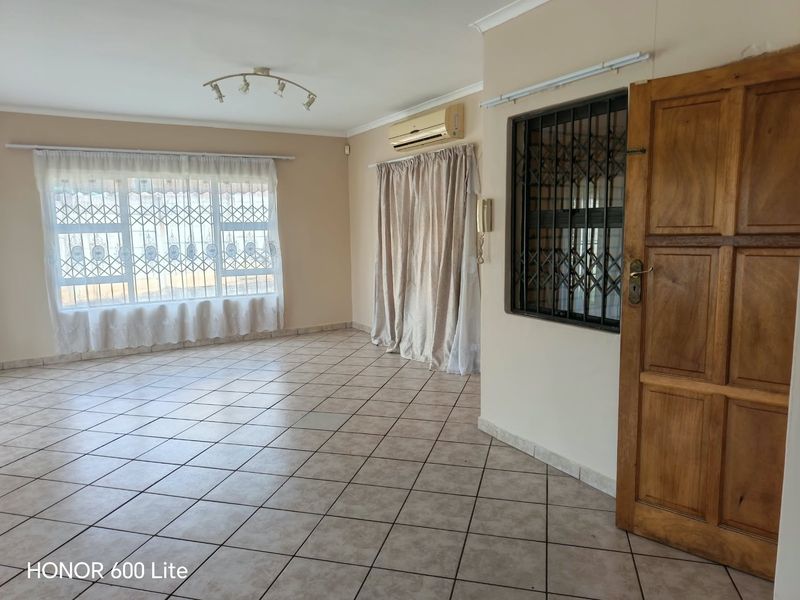 A spacious, empty living area featuring tiled flooring, an air conditioning unit, and secure window treatments, offering a blank canvas for personalization.