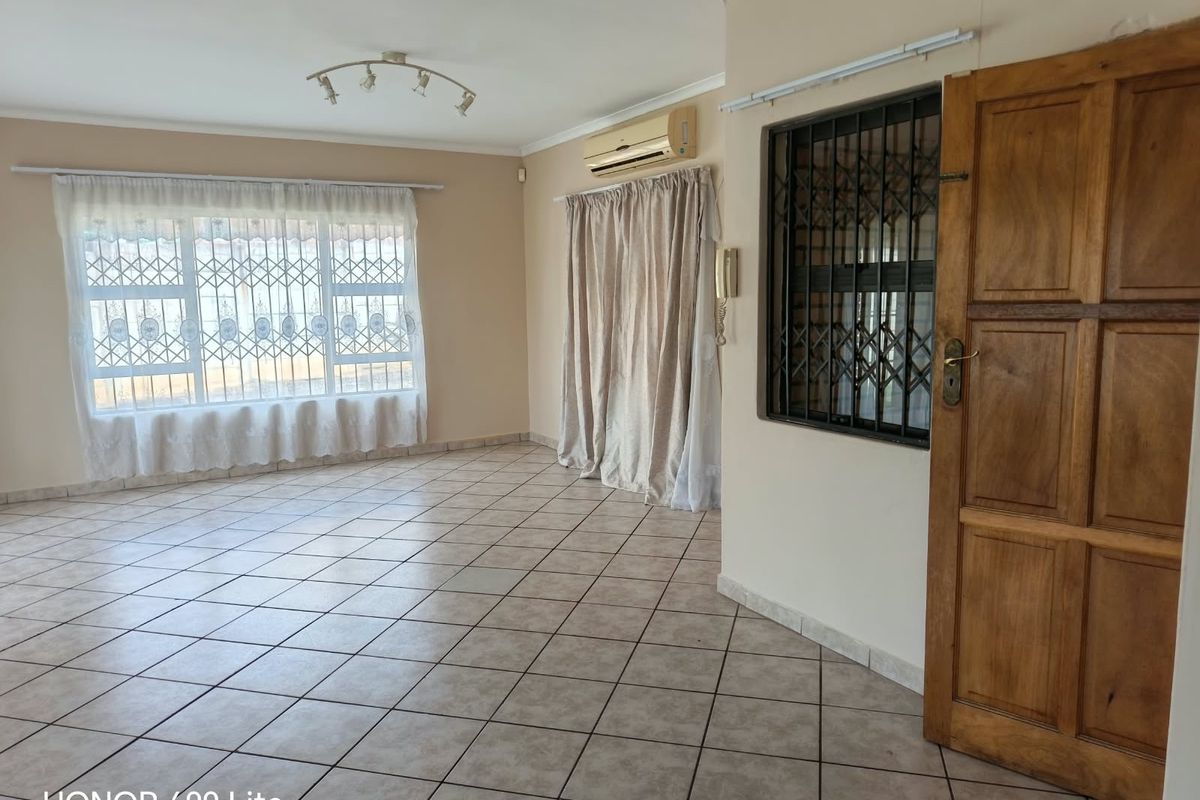 A spacious, empty living area featuring tiled flooring, an air conditioning unit, and secure window treatments, offering a blank canvas for personalization.