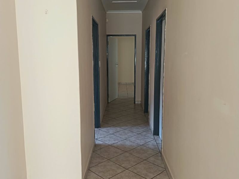 A clean, empty hallway featuring neutral wall paint and diagonal tiled flooring, providing access to multiple rooms.