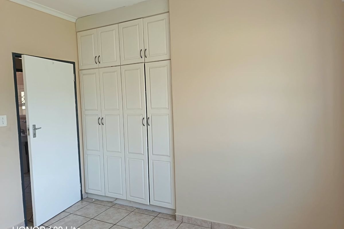 A clean, empty bedroom featuring neutral walls, tiled flooring, and ample built-in cupboard storage space.