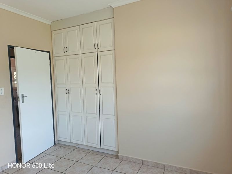 A clean, empty bedroom featuring neutral walls, tiled flooring, and ample built-in cupboard storage space.