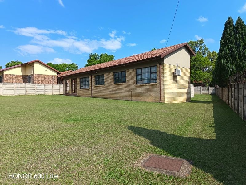Rear view of a face brick house featuring a large lawn, tiled roof, and secure boundary walls.