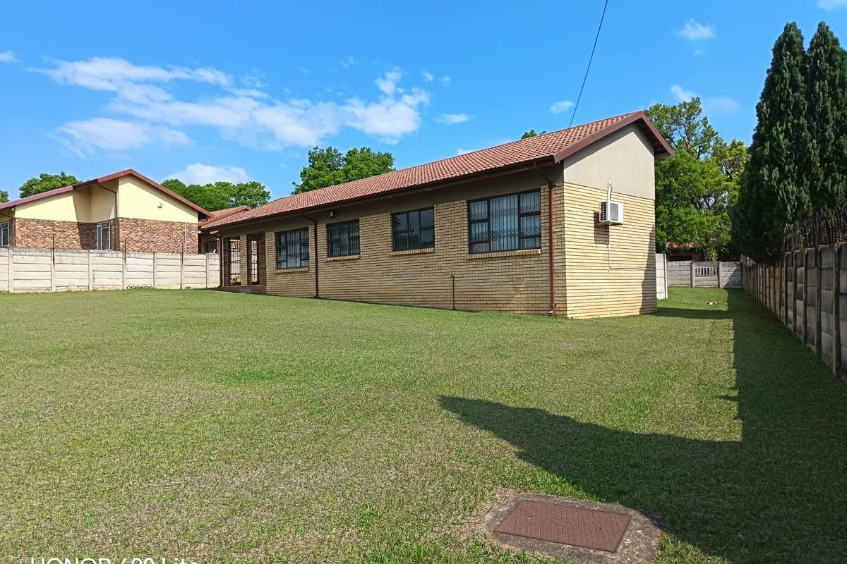 Rear view of a face brick house featuring a large lawn, tiled roof, and secure boundary walls.